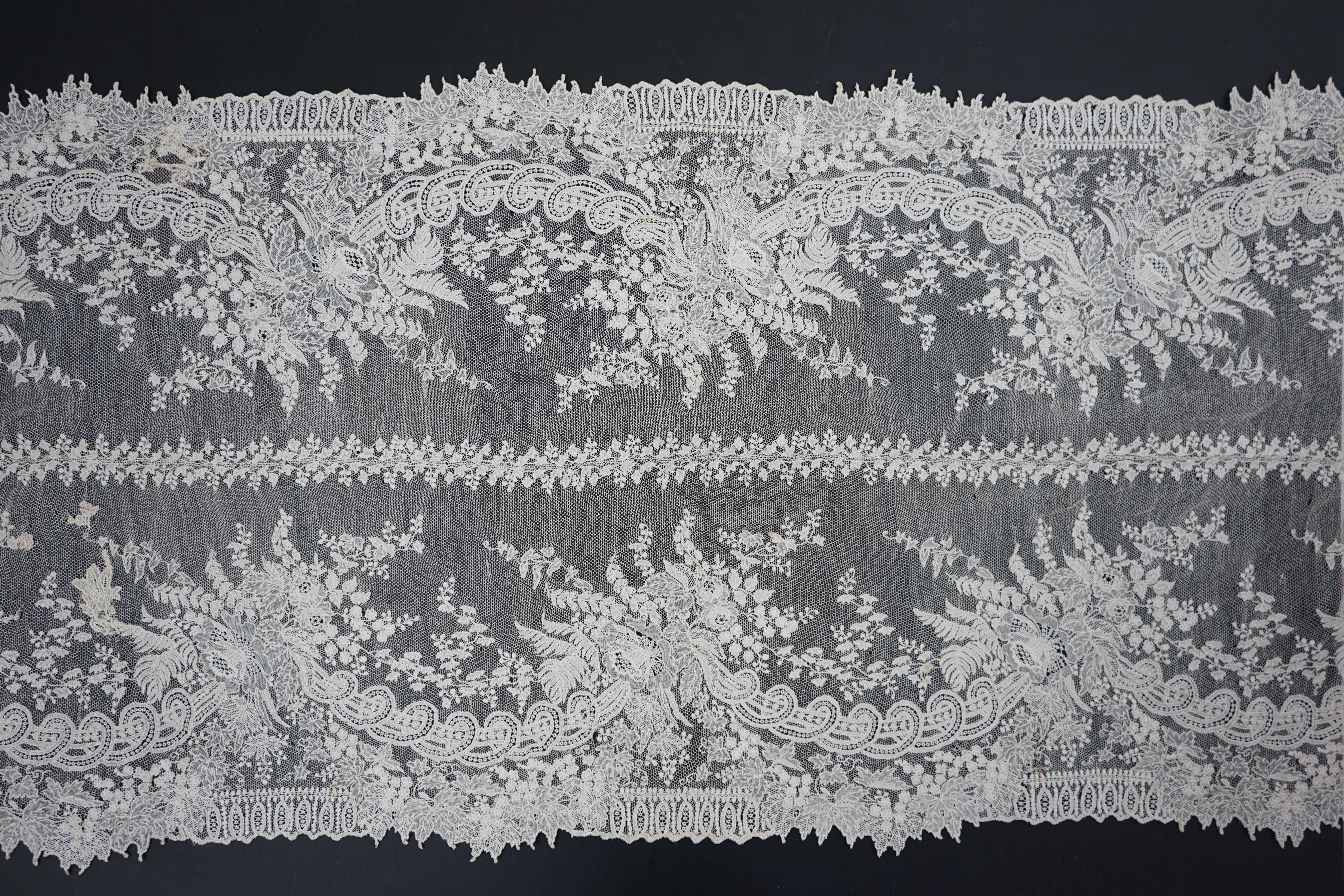 A 19th century Brussels Point de gaze needle lace stole 228cm long x 37cm wide, made from two lengths of the same patterned lace, invisibly joined along the centre of the stole, the raw end edges carefully finished with